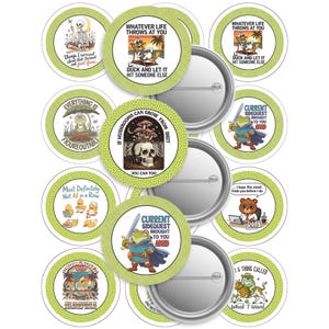 May include: A collection of round, green and white button pins with various illustrations and text. Designs include a skeleton, frog, bear, and mushroom graphic. Text includes "Whatever life throws at you, duck and let it hit someone else."
