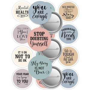 May include: A selection of round pin badges featuring motivational quotes in black script on pastel backgrounds. Phrases include "You are Enough," "Stop Doubting Yourself," and "My Story is Not Over." The badges have a silver metal backing.