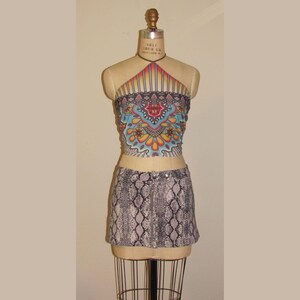 May include: A two-piece outfit on a mannequin. The top is a halter style with a colorful, ornate pattern in shades of blue, orange, and red. The skirt is a mini-skirt with a snakeskin print in gray and black. The outfit is displayed on a vintage dress form.