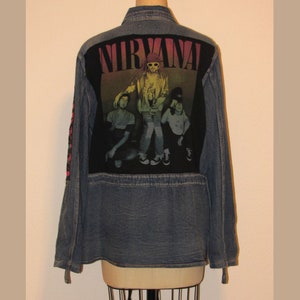 May include: A blue denim jacket with a black patch on the back featuring the band Nirvana and a photo of the band members. The patch has the band's name in rainbow colors.