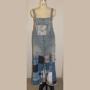 May include: Light blue denim overalls with patchwork detailing on the lower legs. The bib pocket features a floral print. The overalls are displayed on a mannequin.