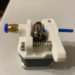 May include: A white 3D printed extruder with a black gear, a silver spring, and a brass fitting with a blue o-ring.