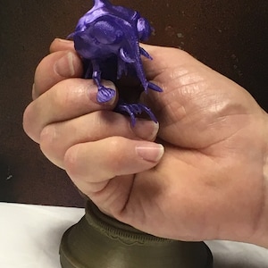 Peut inclure: Une figurine en 3D imprimée en violet d'une créature avec un long bec et des griffes acérées, debout sur une base brune.