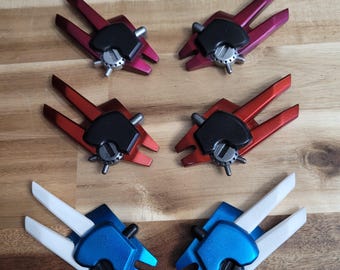 May include: Four pairs of plastic wings in different colors. The wings are red, pink, blue, and white. Each pair has a black center piece with a silver gear.