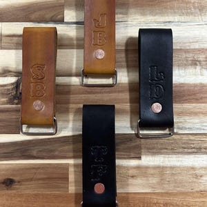 May include: Four leather belt loops with metal rings. The loops are brown and black and have initials embossed on them. The initials are "J.B.", "S.B.", "L.D.", and "T.F."