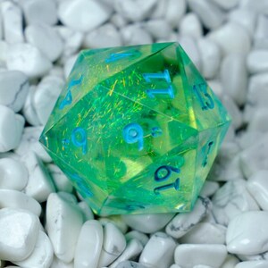 K&ouml;nnte beinhalten: Ein durchscheinender gr&uuml;n-gelber D20-W&uuml;rfel mit blauen Zahlen. Der W&uuml;rfel befindet sich vor einem Hintergrund aus wei&szlig;en Steinen. Der W&uuml;rfel ist ein zwanzigseitiges Polyeder, das &uuml;blicherweise in Tabletop-Rollenspielen verwendet wird.
