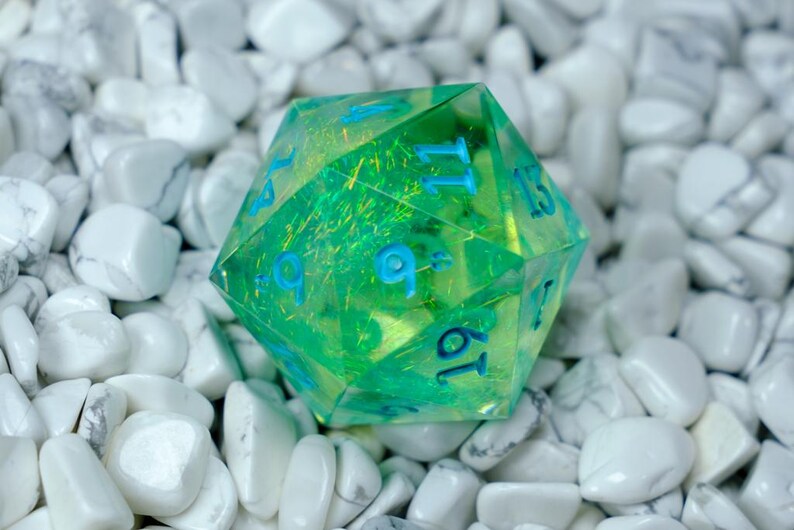 K&ouml;nnte beinhalten: Ein durchscheinender gr&uuml;n-gelber D20-W&uuml;rfel mit blauen Zahlen. Der W&uuml;rfel befindet sich vor einem Hintergrund aus wei&szlig;en Steinen. Der W&uuml;rfel ist ein zwanzigseitiges Polyeder, das &uuml;blicherweise in Tabletop-Rollenspielen verwendet wird.