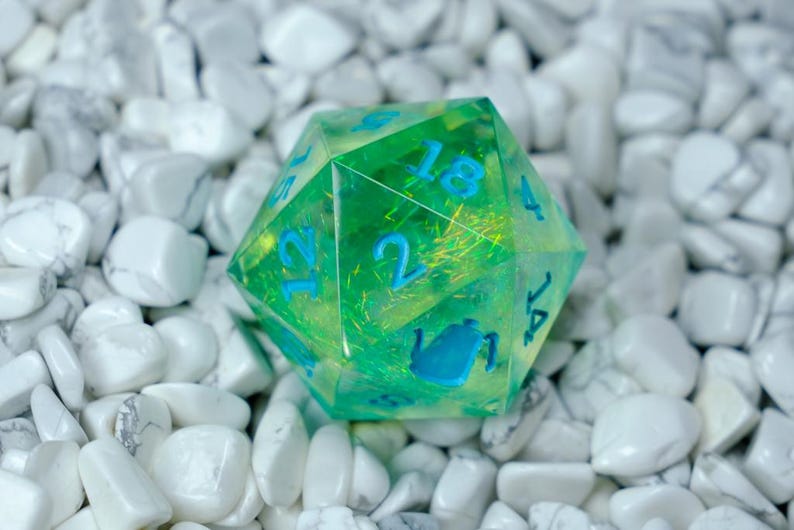 K&ouml;nnte beinhalten: Ein durchscheinender gr&uuml;n-gelber zwanzigseitiger W&uuml;rfel mit blauen Zahlen und Teekannen-Symbolen. Der W&uuml;rfel liegt vor einem Hintergrund aus wei&szlig;en Steinen. Dieser einzigartige W&uuml;rfel ist perfekt f&uuml;r Tabletop-Spiele. Der W&uuml;rfel hat einen Durchmesser von ca. 3 cm.