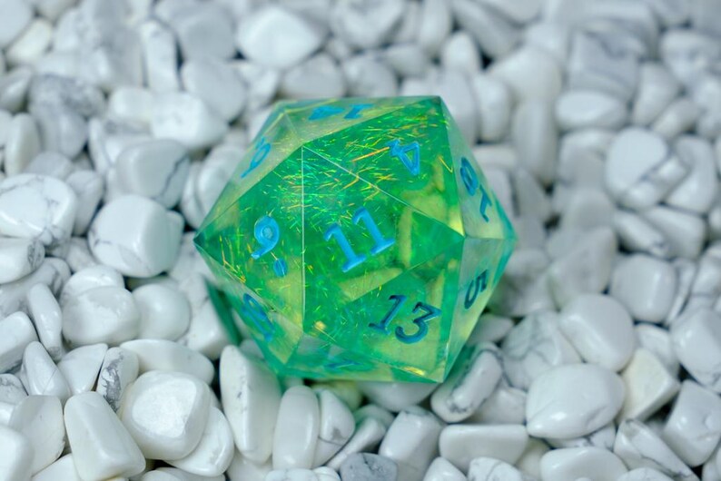 K&ouml;nnte beinhalten: Ein durchscheinender gr&uuml;n-gelber polyedrischer W&uuml;rfel mit blauen Zahlen. Der W&uuml;rfel liegt vor einem Hintergrund aus wei&szlig;en Steinen. Der W&uuml;rfel ist ein Spielzubeh&ouml;r, wahrscheinlich f&uuml;r Tabletop-Rollenspiele.