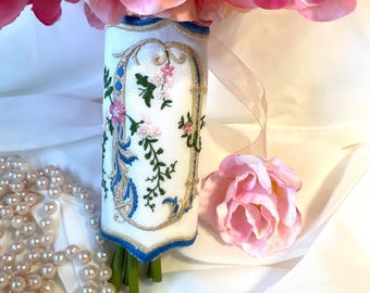 May include: A white fabric bouquet wrap with blue and gold embroidery of a floral design and the letter "O".