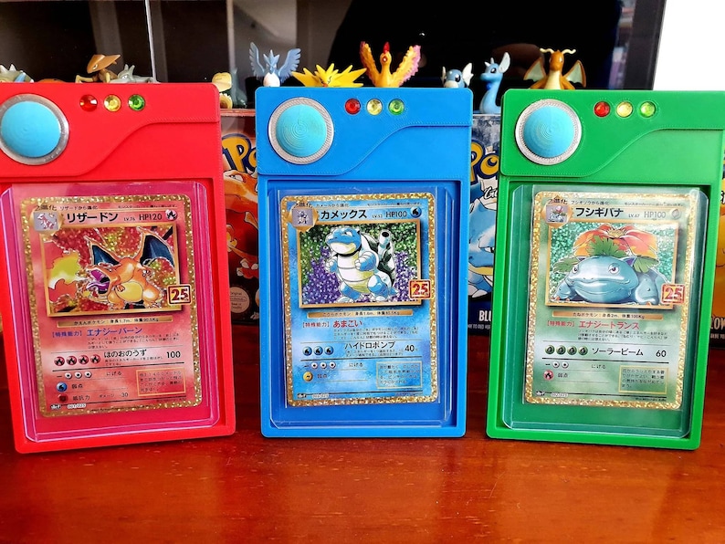 May include: Three Pokemon trading cards, each encased in a plastic protector with a red, blue, and green frame. The cards feature the Pokemon Charizard, Blastoise, and Venusaur, respectively. The cards are from the Japanese version of the Pokemon Trading Card Game.