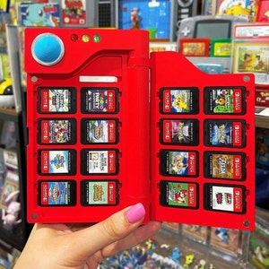 May include: A red Nintendo Switch game card carrying case with a variety of game cartridges inserted. The case has a flip-top lid and a clear plastic window to view the cartridges. The case is designed to hold up to 12 game cartridges.