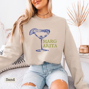 May include: A sand-colored sweatshirt with a blue and green graphic of a margarita glass with the text "Margarita" on it.