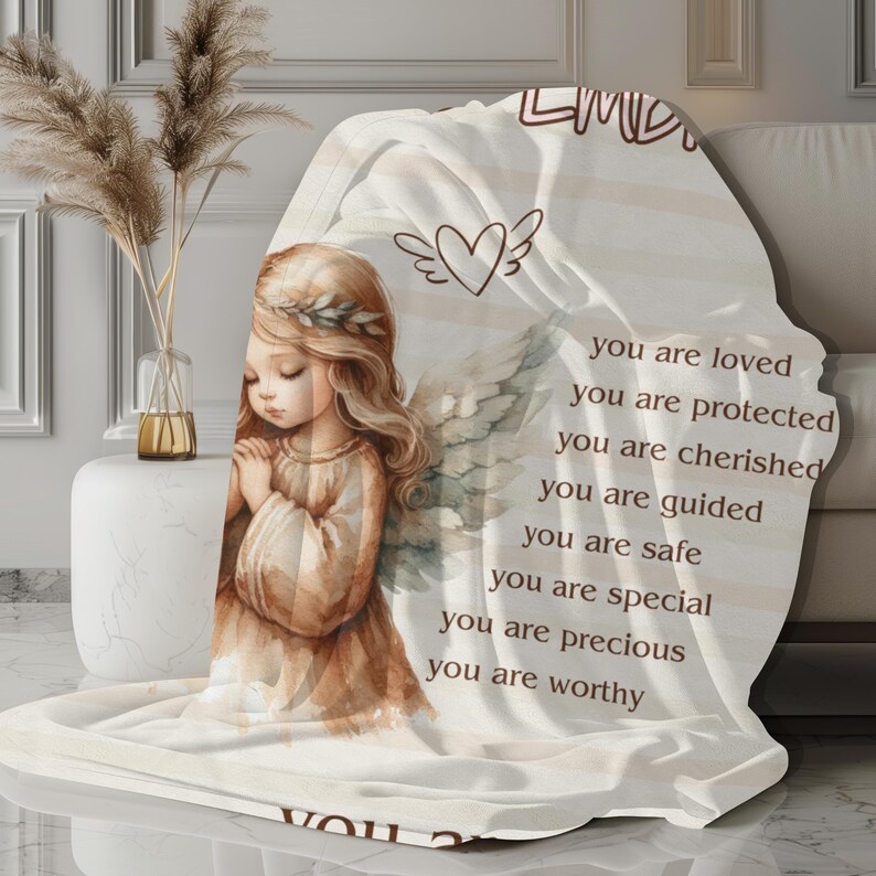 May include: A white throw blanket with a watercolor illustration of an angel with wings and the text "You are loved, you are protected, you are cherished, you are guided, you are safe, you are special, you are precious, you are worthy."