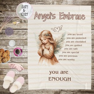 May include: A soft and cozy throw blanket with a white background and a brown angel illustration. The text "Angel's Embrace" is at the top of the blanket. The text "you are loved, you are protected, you are cherished, you are guided, you are safe, you are special, you are precious, you are worthy, you are ENOUGH" is printed on the blanket.