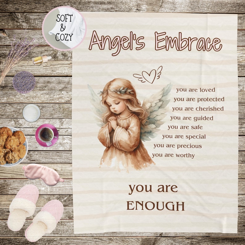 May include: A soft and cozy throw blanket with a white background and a brown angel illustration. The text "Angel's Embrace" is at the top of the blanket. The text "you are loved, you are protected, you are cherished, you are guided, you are safe, you are special, you are precious, you are worthy, you are ENOUGH" is printed on the blanket.