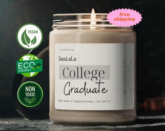 May include: A lit candle in a glass jar with a silver lid. The label reads "Scent of a College Graduate" with the text "Sweet Aroma of Congratulations...You Did It!". The candle has vegan, eco-friendly, and non-toxic labels.