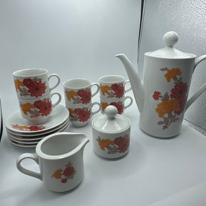 May include: A vintage floral tea set with a teapot, creamer, sugar bowl, and six cups and saucers. The set features a white background with a floral pattern in shades of orange, red, and brown.