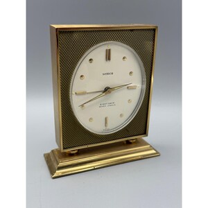 May include: A vintage gold-toned Semca clock with a rectangular frame and a round clock face. The clock face is white with black hands and markers. The text "SEMCA" and "EIGHT DAYS SEVEN JEWELS" are visible.