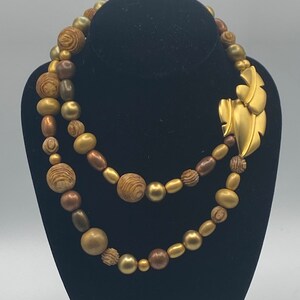 May include: A double strand necklace made of gold and brown beads with a gold leaf pendant.