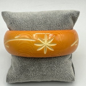 May include: A vintage orange plastic bangle bracelet with a carved white flower design.