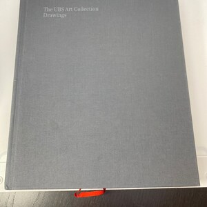 May include: A gray hardcover book with the title "The UBS Art Collection Drawings" and the UBS logo on the front cover.
