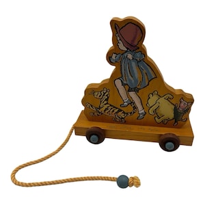 May include: Wooden pull toy featuring a child figure and cartoon characters. The toy is painted in various colors, including yellow, blue, and red. It has a rope for pulling and is mounted on a wooden base with wheels.