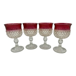 May include: Four clear wine glasses with ruby red rims and diamond-cut patterned bowls. The glasses have clear stems and round bases, creating a classic and elegant look. Perfect for serving wine at a dinner party or special occasion.