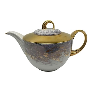 May include: Elegant porcelain teapot with a gold handle, lid, and accents. The body of the teapot features a marbled design in shades of gray, purple, and white, with gold leaf detailing. The spout is white.