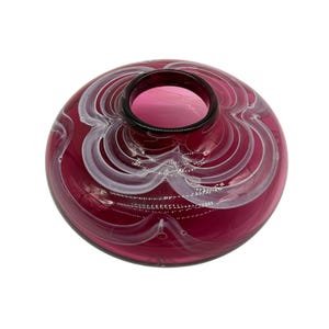 May include: A small, round, burgundy glass vase with white swirls. The vase has a wide opening and a smooth, glossy finish.