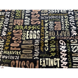 May include: Black fabric with a repeating pattern of white, brown, and green words related to dinosaurs, including "fossils", "eggs", "dinosaur", "raptor", "herbivore", "carnivore", "roar", "extinct", and "Jurassic".