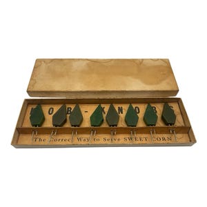 May include: Vintage set of corn holders in a cardboard box. The set includes eight green, leaf-shaped holders with metal prongs. The box has the text "HOB - KNOBS" and "The Correct Way to Serve Sweet Corn."