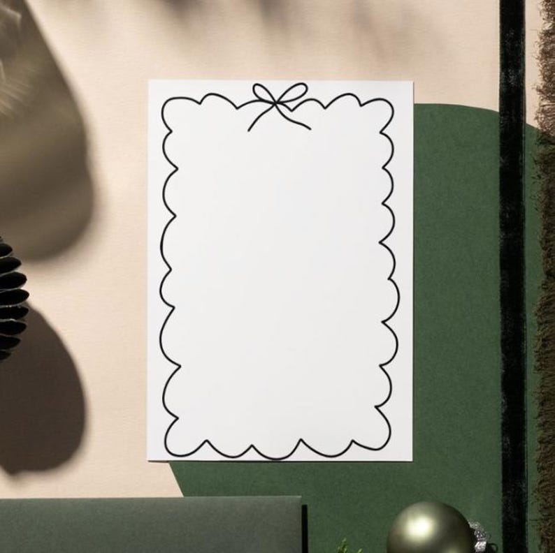 Op de afbeelding: Een witte rechthoekige kaart met een zwarte geschulpte rand en een strik bovenaan. De kaart staat tegen een achtergrond van groene en beige tinten, met een vleugje decoratief element links.