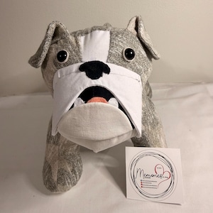 May include: A stuffed bulldog toy with gray and white patterned fabric. The bulldog has black eyes, a black nose, and a white muzzle. A small white card with the word "Memories" in script is in the lower right corner.