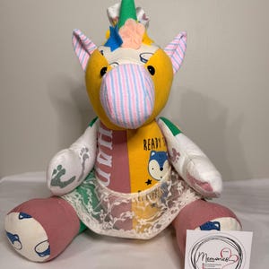 Può includere: Un peluche a forma di unicorno realizzato con vari pezzi di tessuto a fantasia nei colori giallo, rosa e bianco. Presenta un corno verde, un bordo in pizzo intorno alla vita e una stampa di una volpe con il testo READY TO EXPLORE sul petto.
