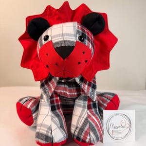 May include: A handmade lion plush toy with a red mane and accents. The lion's body is made from a plaid fabric in red, black, and white. The plush toy has black ears and a red nose. A small white square with the word "Memories" is on the right.