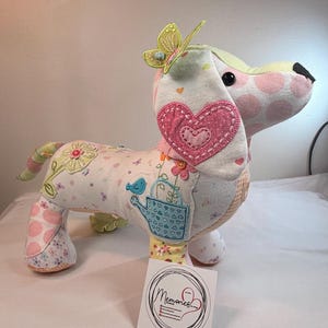 May include: A handmade stuffed dachshund dog made from patchwork fabric in pastel shades. The dog has a pink heart on its ear, a butterfly on its head, and a watering can design. A tag with the word "Memories" is visible.