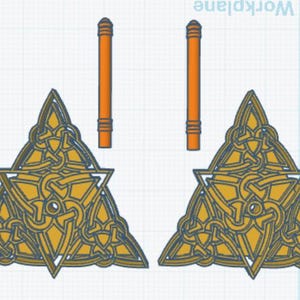 May include: Two gold-colored triangular Celtic knot designs with intricate patterns. Each design is topped with a thin, orange, cylindrical rod.