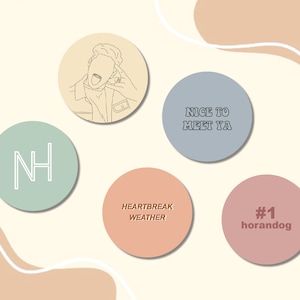 May include: Five round stickers with different designs. The first sticker is light brown with a line drawing of a person with their tongue sticking out. The second sticker is light blue with the text "NICE TO MEET YA". The third sticker is light green with the letters "NH" in white. The fourth sticker is light orange with the text "HEARTBREAK WEATHER". The fifth sticker is light pink with the text "#1 horandog".
