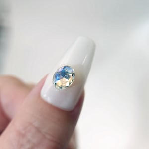 May include: A white oval-shaped nail with a clear iridescent gemstone on top.