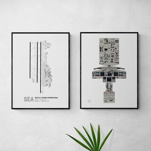May include: Two framed prints on a white wall. The print on the left shows a black and white diagram of Seattle-Tacoma International Airport with the airport code "SEA" and the airport name "Seattle-Tacoma International" below the diagram. The print on the right shows a black and white diagram of an airplane cockpit.