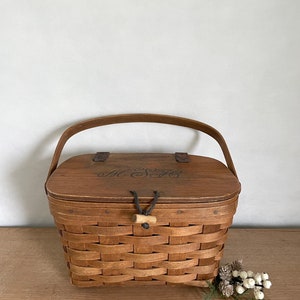 May include: A brown wicker basket with a wooden lid and a leather handle. The lid has the initials "M.S." engraved on it.