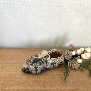 Puede incluir: Un pequeño zapato decorativo de cerámica con una base blanca y un patrón geométrico colorido. El zapato está sobre una superficie de madera con una rama de vegetación y bayas blancas.