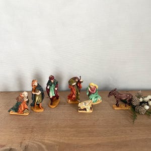May include: A nativity scene set with eight figurines, including the three wise men, Mary, Joseph, baby Jesus, a donkey, and a shepherd. The figurines are made of painted ceramic and are standing on a wooden surface.