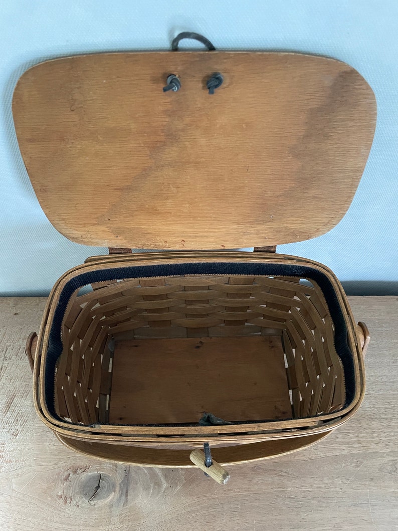May include: A wooden basket with a hinged lid and a black fabric lining. The basket has two handles and a wooden latch.
