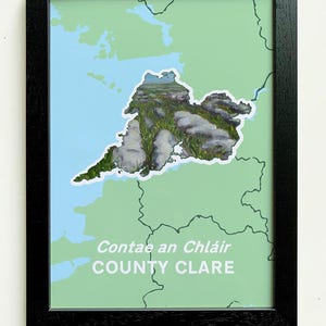 May include: A framed print of a map of County Clare, Ireland. The map is green with a white outline of the county. The center of the map is a photo of a rocky landscape with green grass.