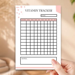 May include: A white paper vitamin tracker sheet with black grid lines, featuring the text VITAMIN TRACKER at the top, a week field, columns for vitamin, dose, time, and days of the week, and a notes section at the bottom with light pink accents.