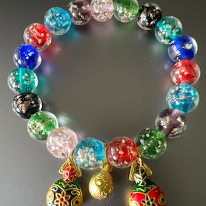 May include: A colorful glass bead bracelet with three gold charms. The beads are clear with flecks of gold, silver, and other colors. The charms are shaped like fish and have red, green, and blue enamel details.