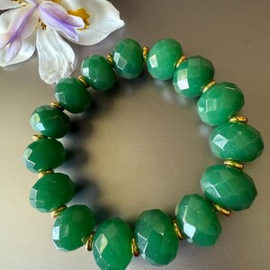 May include: A green gemstone bracelet with gold accents. The bracelet is made of faceted beads and is strung on an elastic cord.