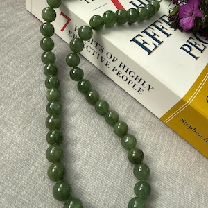 May include: A green jade bead necklace and bracelet set. The beads are round and have a polished finish. The necklace is draped over a book titled "The 7 Habits of Highly Effective People".